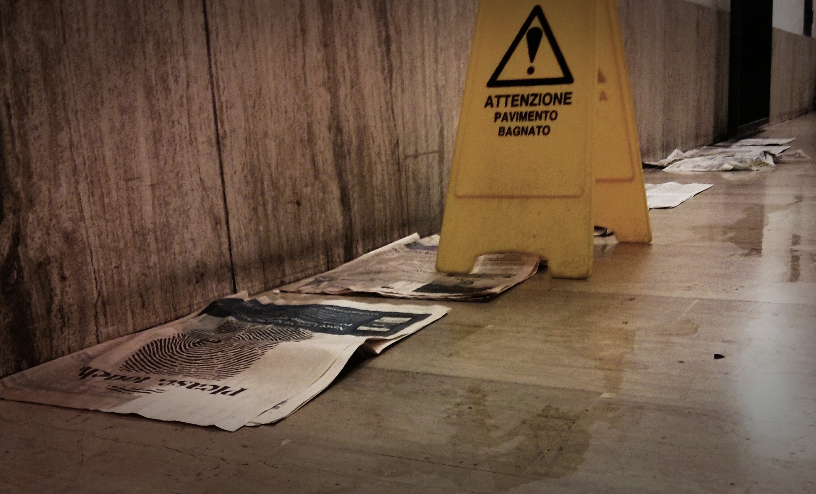 Zeitungen saugen in der Bahnhofsunterführung von Perugia Wasser auf dem Boden auf, daneben ein Warnschild